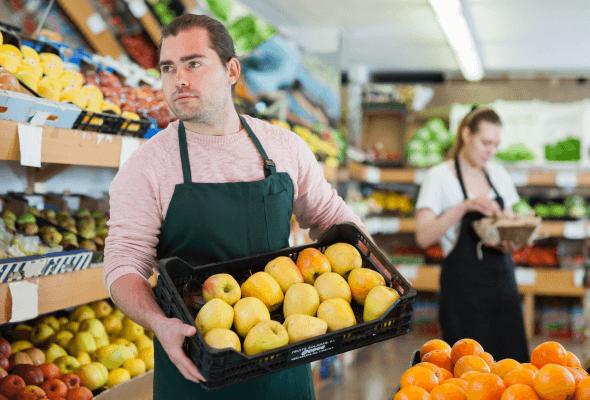 Shop assistant carrying a crate of apples